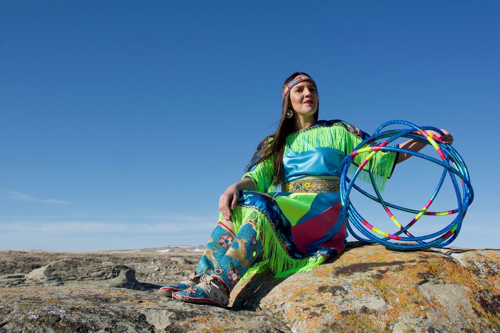 Photograph of Sandra Lamouche wearing regalia, holding hoops in her left hand and looking into the distance.