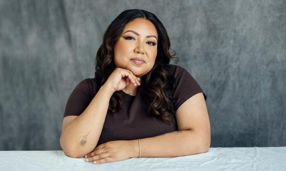 Joelle's headshot with her hand to her shin in front of a grey background.
