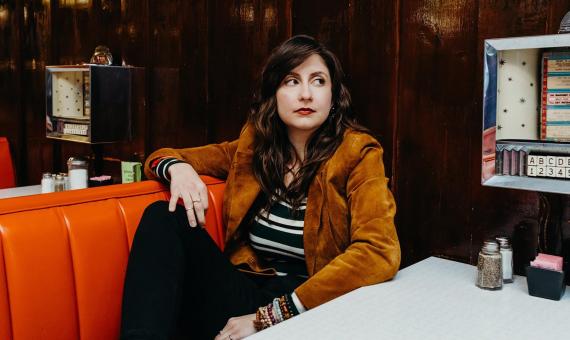 Headshto of artist and programmer Katey Gatta sitting in an old diner.