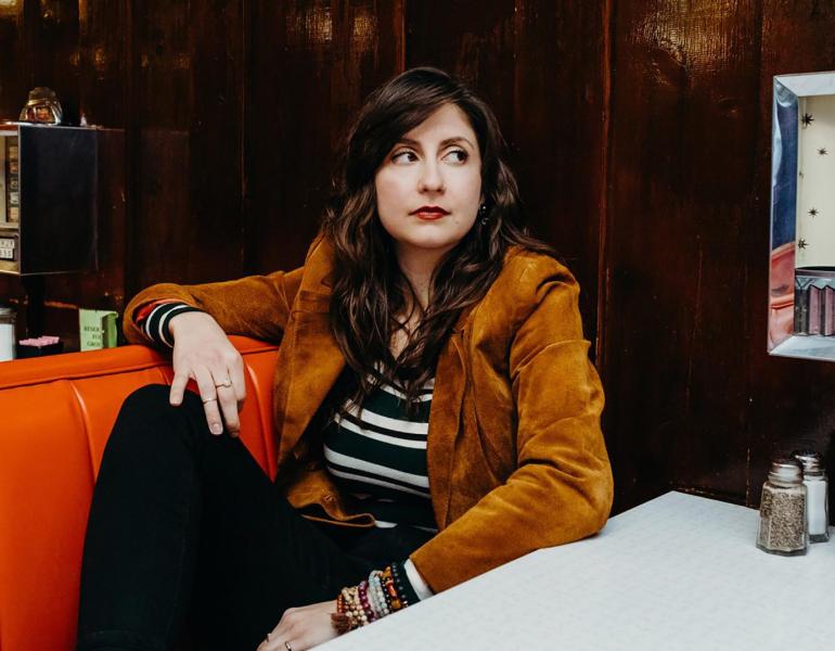 Headshto of artist and programmer Katey Gatta sitting in an old diner.