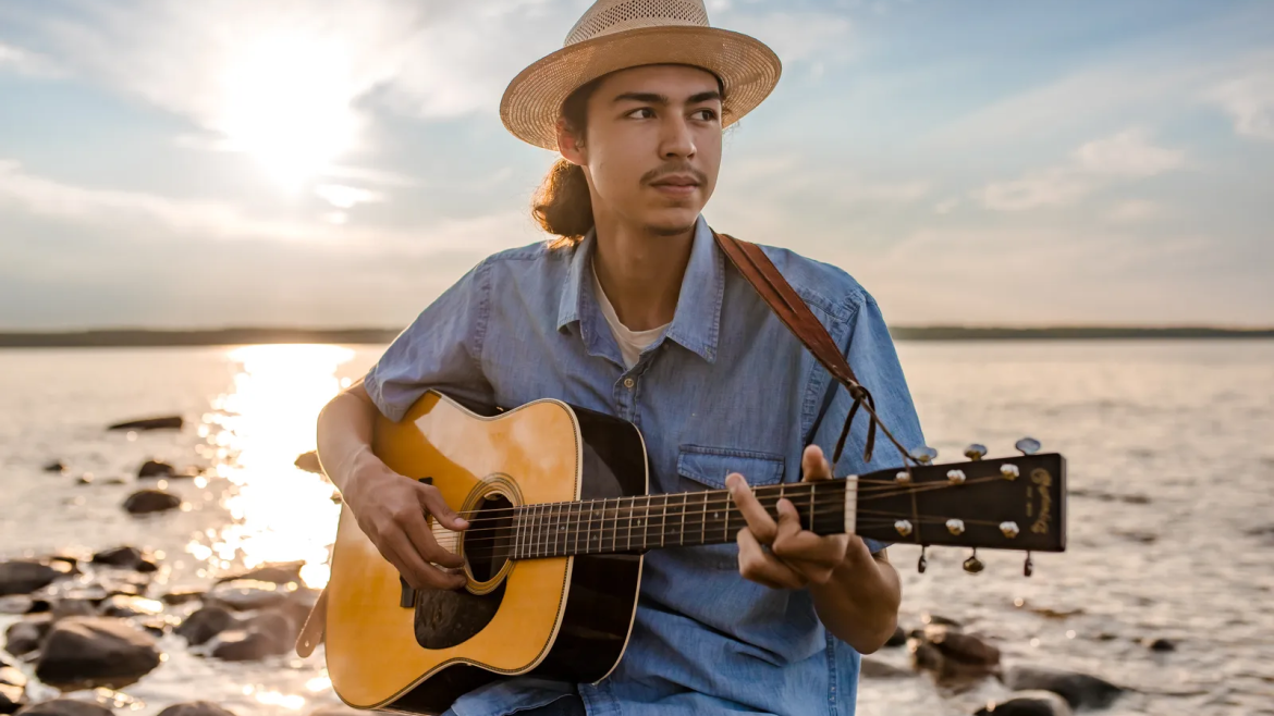 JD Crosstown with a guitar in front of the water on the shoreline.