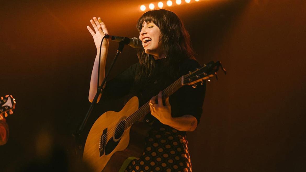 Katey performing with a guitar on stage with moody lighting.